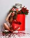 Happy brunette girl celebrate valentines day or birthday party sitting at big box with flowers holding red heart balloon Royalty Free Stock Photo