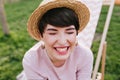 Happy brunette girl in trendy summer hat and cute earrings laughing with eyes closed. Fascinating young woman with short