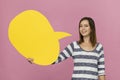 Young woman with smile holding blank yellow speech bubble against pink background