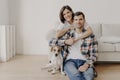 Happy brunette woman embraces husband with love, being in good mood, smiles positively. Husband, wife and dog pose together in