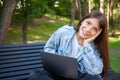 Happy brunette young girl freelancer sitting on bench in park with laptop Royalty Free Stock Photo