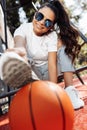 Happy brunette young woman dressed in casual modern clothes and sunglasses posing with basketball at the stadium. Royalty Free Stock Photo