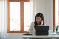 Happy business asian manageress working at her desk in the office taking a call on her mobile phone while writing notes