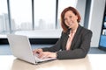 Happy business woman with red hair smiling at work typing on computer laptop at modern office desk Royalty Free Stock Photo