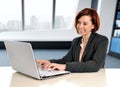 Happy business woman with red hair smiling at work typing on computer laptop at modern office desk