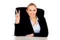 Happy business woman sitting behind the desk and shows victory sign Royalty Free Stock Photo