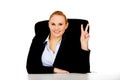 Happy business woman sitting behind the desk and shows victory sign Royalty Free Stock Photo