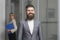 Happy businessman with blurred woman on background. Bearded man in formal suit in office. Confident man smile with beard Royalty Free Stock Photo