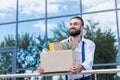 Businessman with cardboard box with office supplies in hands standing outside office building, quitting job concept