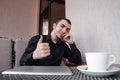 Happy businessman with digital tablet makes a gesture thumb up in the cafe and drink cup of coffee. Royalty Free Stock Photo