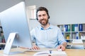 Happy businessman with headset for video call working in modern office, smiling man looking at computer monitor Royalty Free Stock Photo