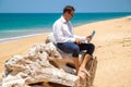 Happy businessman in shirt with a laptop and with glasses walking on the beach.