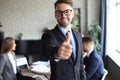 Happy businessman showing his thumb up with colleagues in the background in office Royalty Free Stock Photo