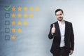 Happy businessman showing thumbs up to 5 star rating on concrete wall background. Customer service and excellent feedback Royalty Free Stock Photo