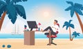 Happy businessman sitting with feet at office table on sand beach of paradise island Royalty Free Stock Photo