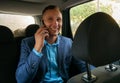 Happy businessman sitting in luxury car. Young bearded man wearing business suit using his smartphone. Royalty Free Stock Photo