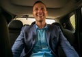 Happy businessman sitting in luxury car. Young bearded man wearing business suit using his smartphone. Royalty Free Stock Photo