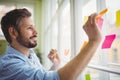 Happy businessman sticking adhesive notes on window at office