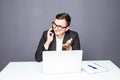 Happy young businessman talking on cell phone and using laptop in office Royalty Free Stock Photo