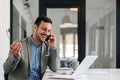 Happy businessman talking on smart phone while sitting at desk in office Royalty Free Stock Photo