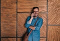 Happy businessman talking on smart phone while standing against brown wall Royalty Free Stock Photo