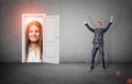 A happy businessman in victory motion stands in a room with a white door opening to a giant happy female face. Royalty Free Stock Photo