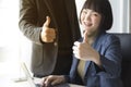 Businesswoman and businessman showing thumbs up sign with computer on wooden table in office background. Royalty Free Stock Photo