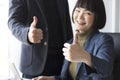 Businesswoman and businessman showing thumbs up sign with computer on wooden table in office background. Royalty Free Stock Photo