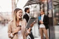 Happy businesswoman holding digital tablet and coffee to go outside of modern building, businesspeople in background Royalty Free Stock Photo