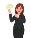 Happy businesswoman showing or holding cash, money, dollar, currency notes in hand and pointing, gesturing hand. Modern lifestyle.