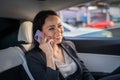 Happy businesswoman sitting in the back seat of a car while using smartphone and talking . Business, road trip