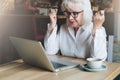 Happy businesswoman sitting in cafe at table in front of laptop,holding hands up and looking at monitor.Good news. Royalty Free Stock Photo