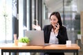 Happy businesswoman sitting at desk behind her laptop and talking with somebody on her mobile phone while working at Royalty Free Stock Photo