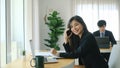 Businesswoman working with computer laptop and talking on mobile phone while sitting with her colleague in modern office. Royalty Free Stock Photo