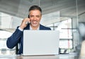 Happy busy middle aged business man talking on phone using laptop in office. Royalty Free Stock Photo