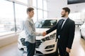 Happy buyer of car shaking hands with seller in auto dealership, in front of car Royalty Free Stock Photo