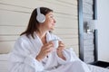 Happy calm mature woman in headphones with cup of coffee listening to audio