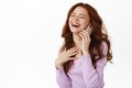 Happy candid girl with red hair laughing calling on phone, talking on smartphone and chuckle something funny, standing