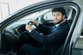 Happy car owner at the dealership. Handsome young men sitting at front seat of the car looking at camera Royalty Free Stock Photo