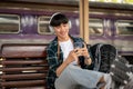 A carefree Asian man backpacker is listening to music while waiting for his train Royalty Free Stock Photo