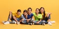 Lovely diverse kids sitting on floor on yellow background