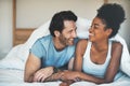 Happy, carefree and laughing couple having fun lying in bed together. Interracial husband and wife bonding and showing Royalty Free Stock Photo