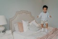 Happy carefree mixed race ethnicity kid boy in casual clothes having fun and jumping on bed Royalty Free Stock Photo