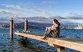 Happy carefree woman sitting on pier on the lake with seagulls enjoying fresh autumn breeze Royalty Free Stock Photo