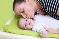 Happy caring mother holding a smiling baby girl and kisses her on changing pad.