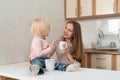 Happy caring mum and little blond girl drink tea at the kitchen. Family breakfast