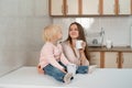 Happy caring mum and little blond girl take a breakfast at the kitchen