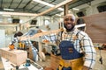 happy carpenter wood enjoy working in large wood workshop. smiling black joiner carrying pile wood making furniture Royalty Free Stock Photo