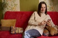 Happy casual beautiful woman using smartphone sitting on sofa at home chatting with friends doing shopping online browsing Royalty Free Stock Photo