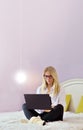Happy casual beautiful woman working on a laptop sitting on the bed in the house Royalty Free Stock Photo